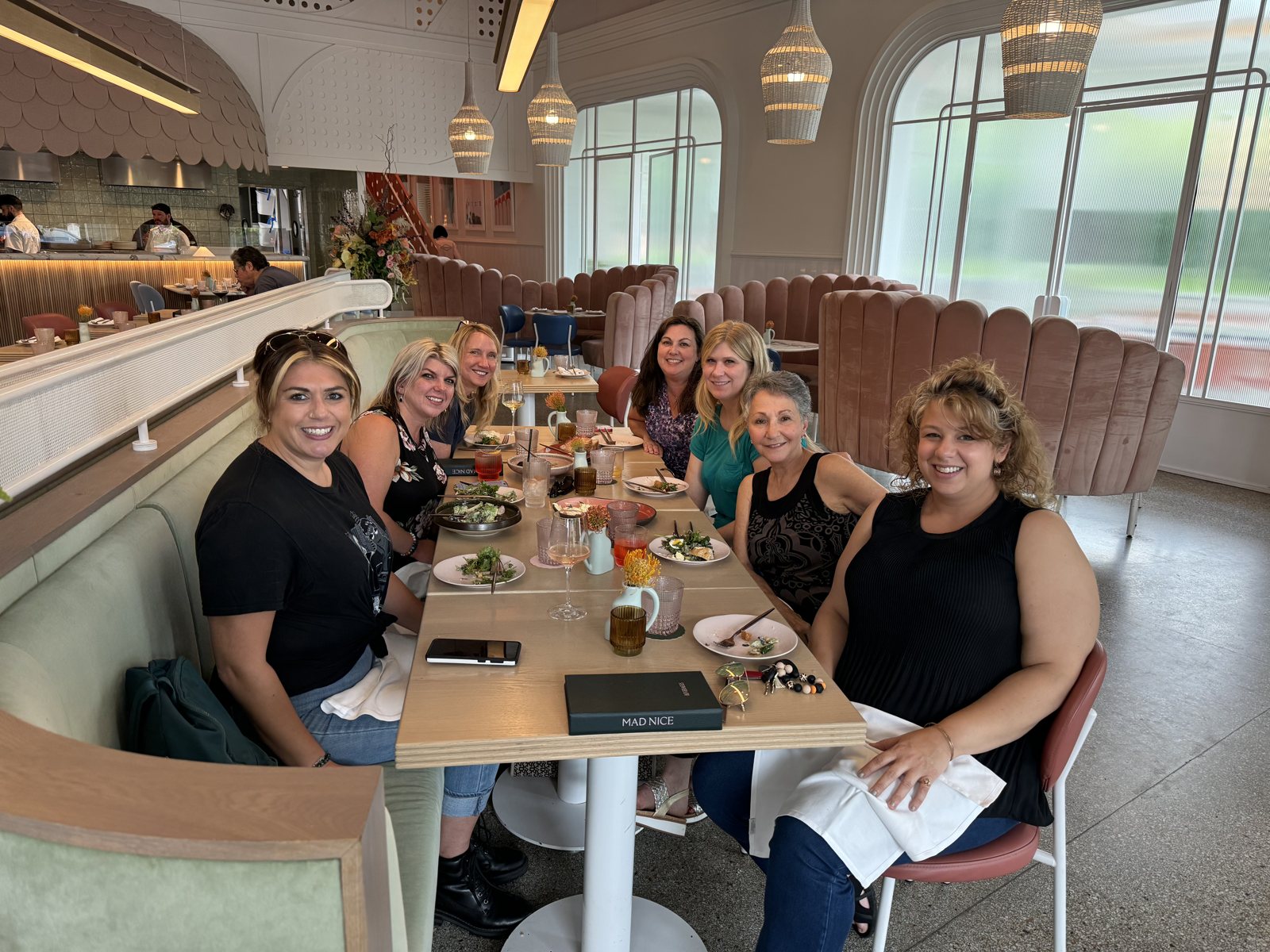 A long table of women gathered together at a Detroit restaurant, smiling at the camera over lunch.