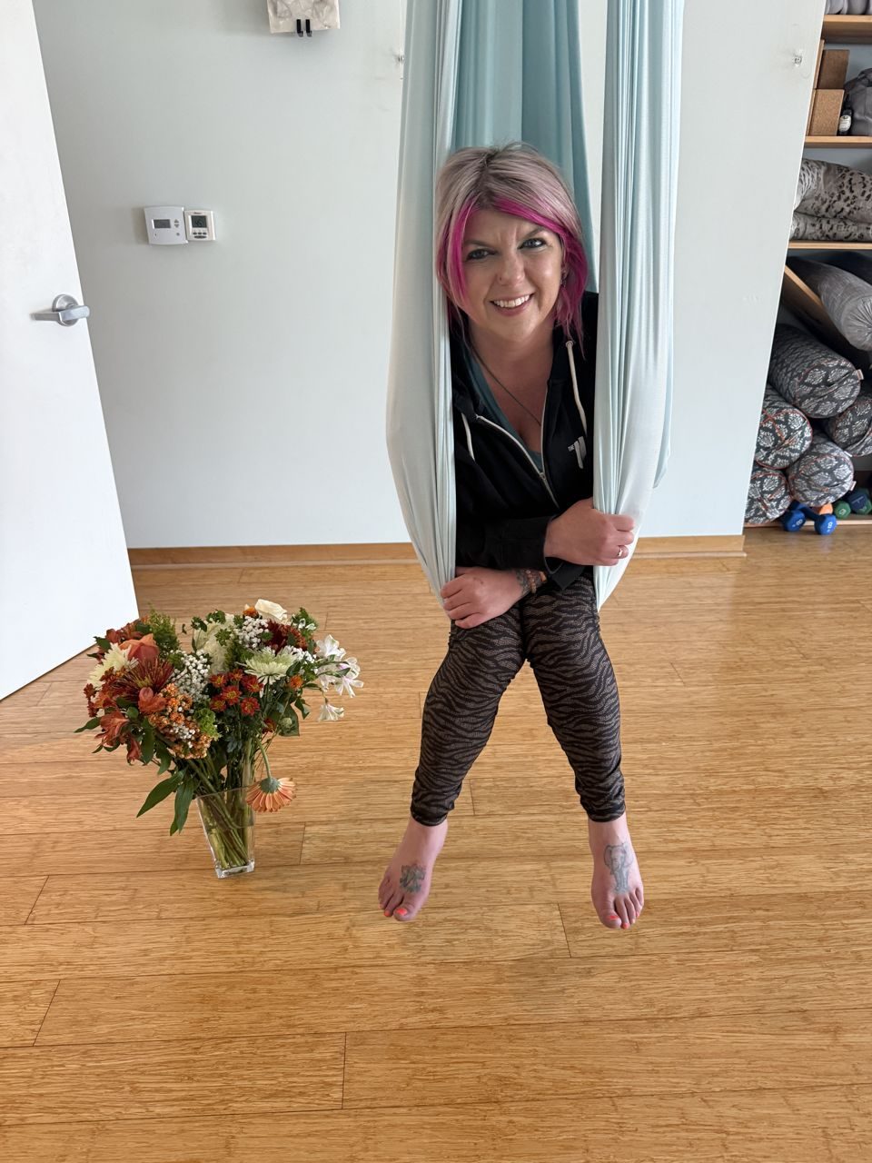 Amanda in an aerial yoga hammock beside a bouquet of flowers